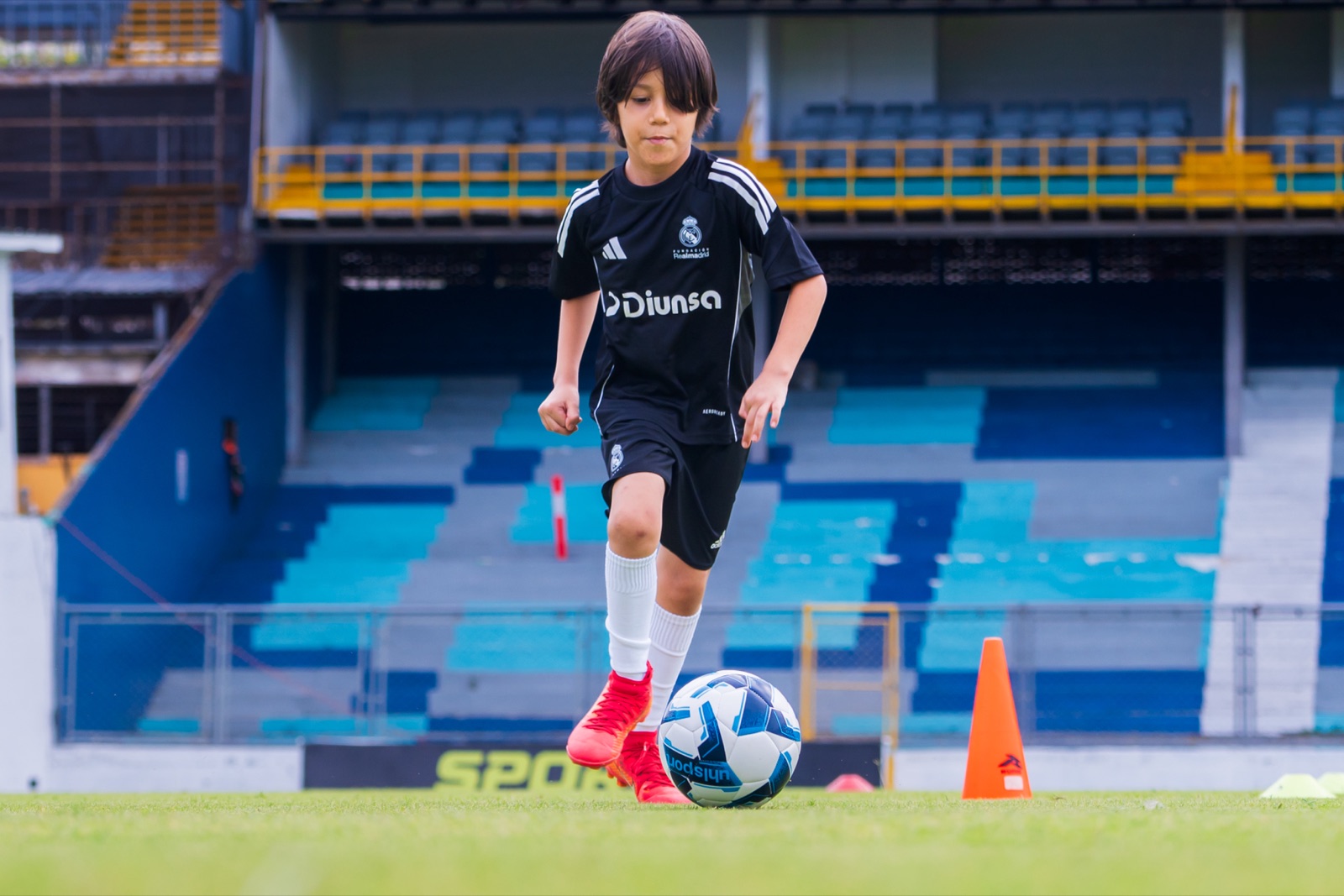 Niño driblando en estadio